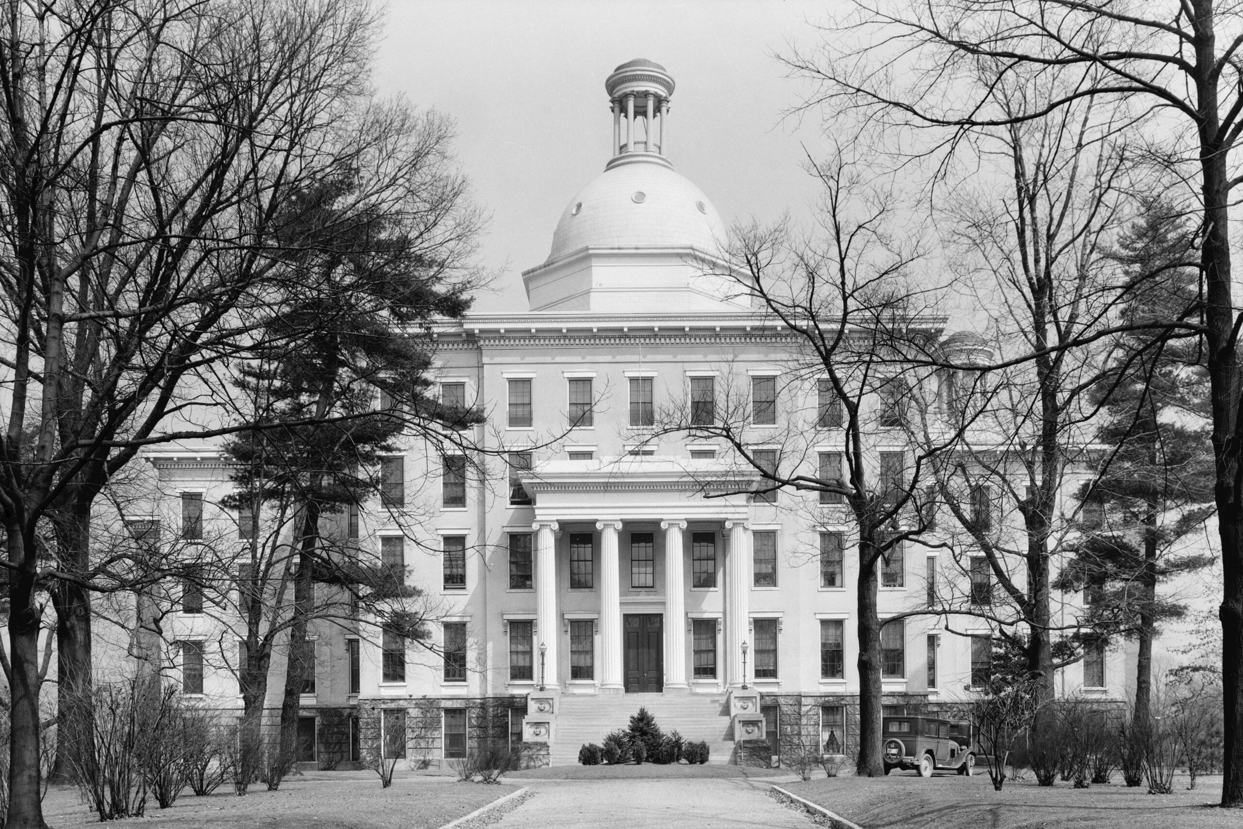 KSB building circa 1934. Large white 5-story building with rotunda topper on top, viewed from end of driveway covered in trees on both sides and U-shaped building wrapped away from photo